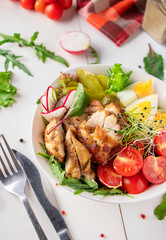 Healthy Buddha bowl lunch with baked chicken, quinoa, cherry tomatoes, radishes, eggs, pickles cucumber, microgreens and arugula on a white background