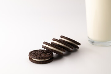 Close-up of a row of chocolate cream cookies next to glass full of milk on an isolated white background.