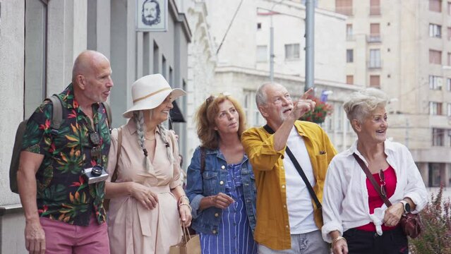 Group of happy senior friends tourists walking in city, laughing.