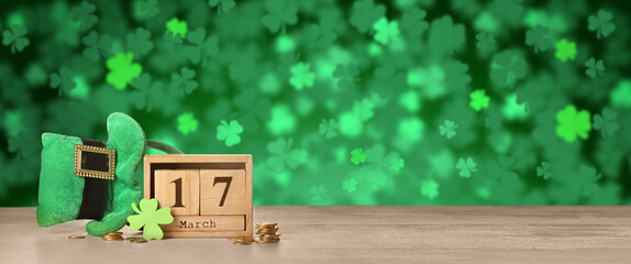 Leprechaun's hat, calendar and coins on table against green background. St. Patrick's Day celebration