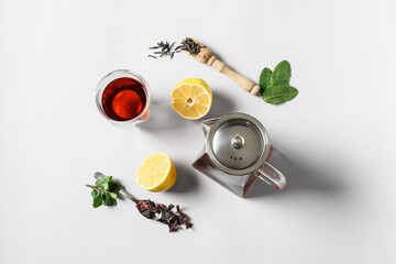 Composition of teapot, glass with tasty tea and lemon on light background