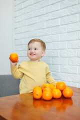 A little boy 2 years old holds tangerines in his hands. The kid wants to sit on citrus fruits for the first time.