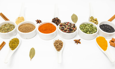 Set of different spices, in ceramic bowls and spoons, for cooking, on a white background.