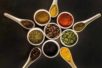 Spices of different varieties, laid out in the shape of a star, in white bowls and spoons, on a gray background, top view.