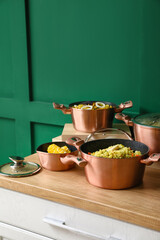 Cooking pots with prepared food on wooden table  near color wall, closeup