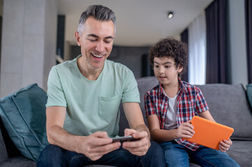 Boy looking at smartphone of man sitting near