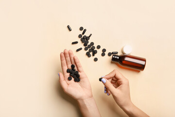 Woman holding activated carbon pills on light background