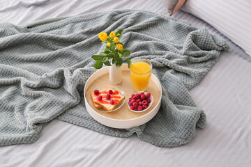 Tray with breakfast and vase with flowers on soft plaid