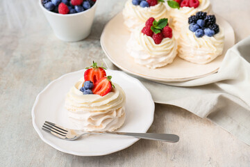 Plates of tasty Pavlova cakes with fresh berries on grunge background