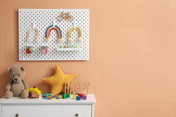 Chest of drawers and peg board with toys hanging on beige wall