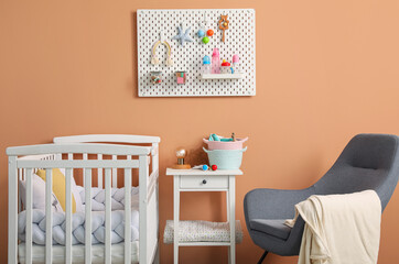 Interior of stylish children's bedroom with crib and hanging pegboard on beige wall
