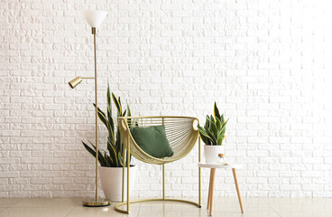 Golden standing lamp, armchair and houseplants near white brick wall