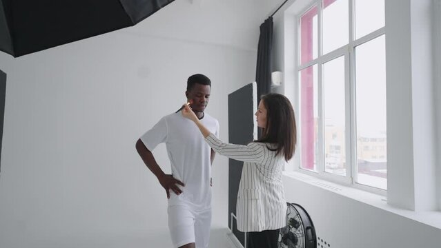 Behind the scenes of a photo shoot: A beautiful black model football player is preparing for a photo shoot for a magazine, a makeup artist corrects the tone of the skin for photos in a sports magazine