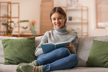 Obraz premium Beautiful young woman with book on sofa at home