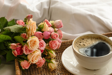 Tray with cup of coffee and bouquet of roses on soft bed, closeup