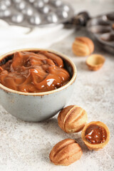 Bowl with boiled condensed milk and walnut shaped cookies on light background