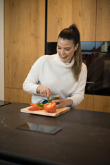 Cute smiling happy woman is preparing a fresh and healthy vegan salad with lots of vegetables in the kitchen at home and trying a new recipe