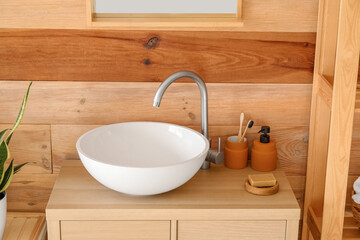 White sink with soap and toothbrushes near wooden wall