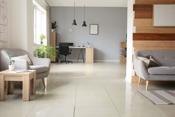 Interior of light living room with grey sofa, armchair and workplace