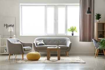 Interior of light living room with grey sofa, armchair and window