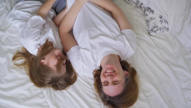 view top. mother and daughter laughs with tickling on the bed. games of children