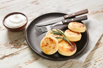 Plate with tasty cottage cheese pancakes and sauce on light wooden background, closeup