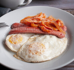Macro photography well done fried eggs with sausage and tomato and onion spicy salsa on a white plate with a fork on the side 