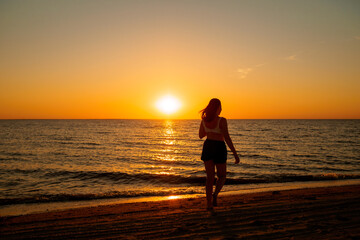 Fototapeta premium Silhouette of a young girl on the seashore against the backdrop of the setting sun.
