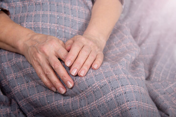 Old woman's hands rest over the plaid. 