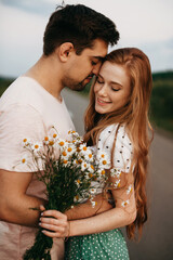 Naklejka premium Couple of lovers in the middle of a country road holding each other by hand. Portrait of a girl with a bouquet of daisies. Beautiful female person. Beautiful