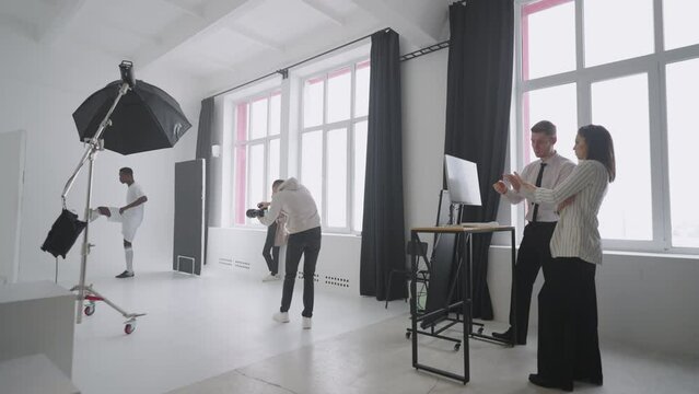 Behind-the-scenes photo shoot: A photographer in a photo studio uses a flash for photos of a black professional football player. Photo shoot in the studio of a sports magazine, advertising