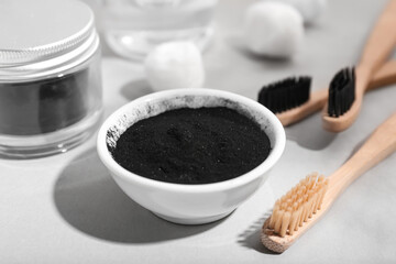 Bowl with activated charcoal tooth powder and toothbrushes on light background, closeup