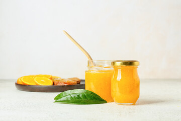 Glass jars of tasty orange jam on light background