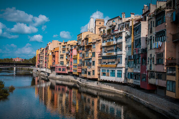 Fototapeta na wymiar Panorama of Girona from the river, looking away from Girona cathedral of Saint Mary and red Eiffel bridge. Greenery on the water is seen.