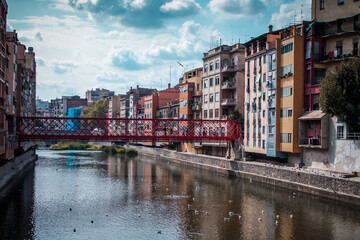 Fototapeta na wymiar Panorama of Girona from the river, looking towards Girona cathedral of Saint Mary and red Eiffel bridge. Greenery on the water is seen.