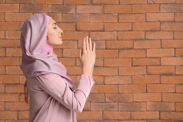 Muslim woman praying on brick background