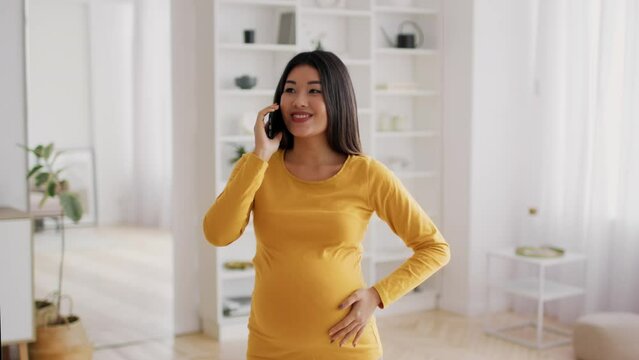Happy Pregnant Young Asian Woman Talking On Mobile Phone At Home