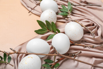 Beautiful Easter eggs, tree branches, leaves and cloth on color background, closeup