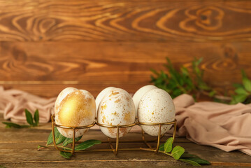 Holder with beautiful Easter eggs and plant leaves on wooden table
