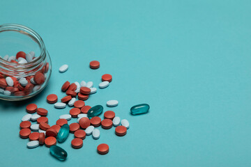 Studio photo of a glass jar of a mixture of medical pills. Some pills spilled out of the jar. The background is blue. 