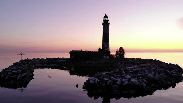Dark silhouette of tower on small artificial island from stones, camera flying back, shows the general perspective of Suho Island on Lake Ladoga. Flat surface of water reflecting shadow of the islet