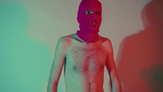 Portrait of anonymous shirtless man in balaclava. Unrecognizable carefree skinny male with naked torso in pink balaclava standing near wall.