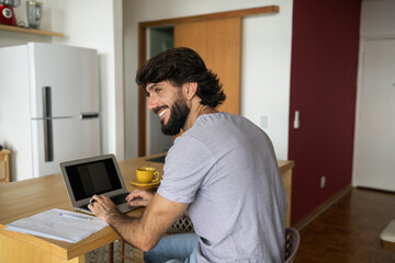 Young business man working at home in his kitchen with laptop and papers on kitchen wooden desk. Home office concept.