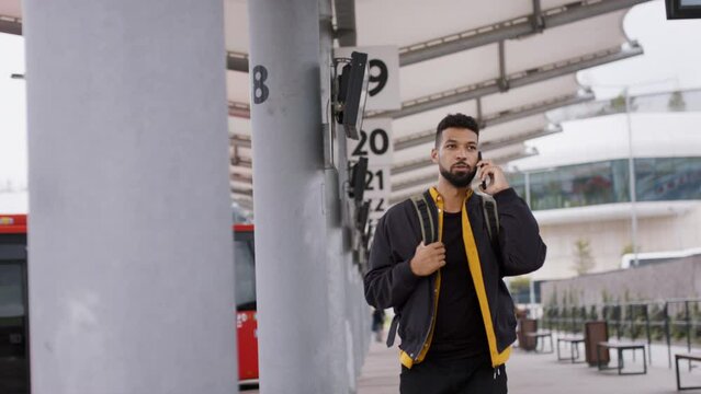 Young African- american man commuter walking in bus station and using smartphone.