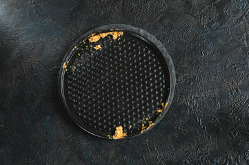 Empty round black baking dish with pie crumbs on a black and blue concrete background. Top view, flat lay with copy space © Tinka Mach