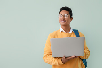 Male African-American student with laptop on color background