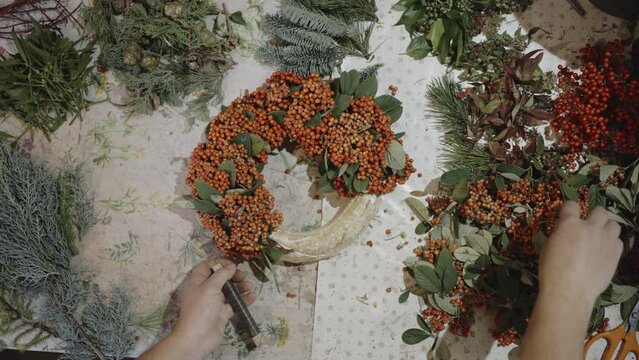 Close up shot of gardeners hands decorating a holiday wreath in red and green, just in time for Christmas