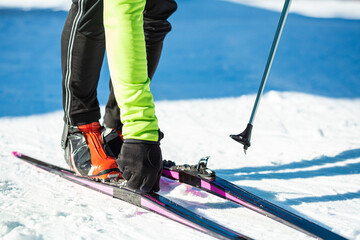 Male professional skier standing on the snow, attaching cross country skis to ski boots, close-up shot.
