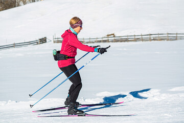Middle aged woman, a recreational cross country skier, rides skis on the empty ski trail in the mountain foothill.