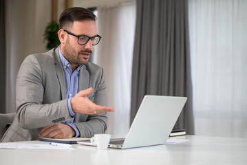 Serious businessman entrepreneur in office making important online video chat conference call, explaining discussing about serious problem opposing confronting other meeting participants